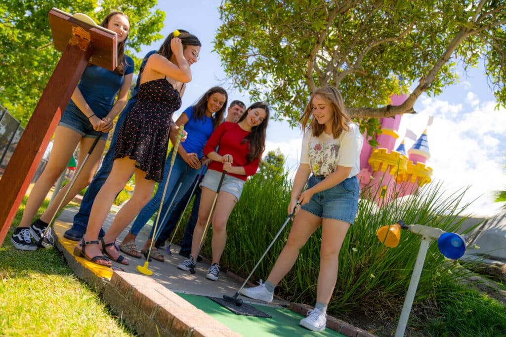 a group of friends play mini golf in front of a pink castle